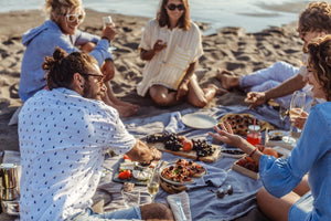 Group of men and women having a hamper picnic on the beach 